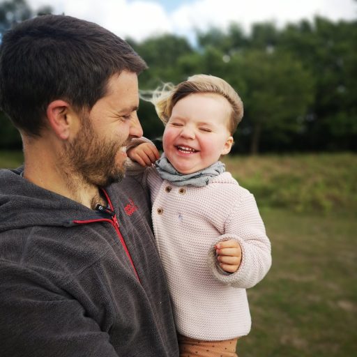 A man holding a small child as they smile and the wind blows through their hair.
