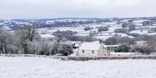 A farm house with a backdrop of fields and hedges in the snow