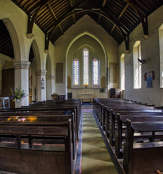 A photograph of the interior of the church showing the pews, stonework, alter and stained glass windows