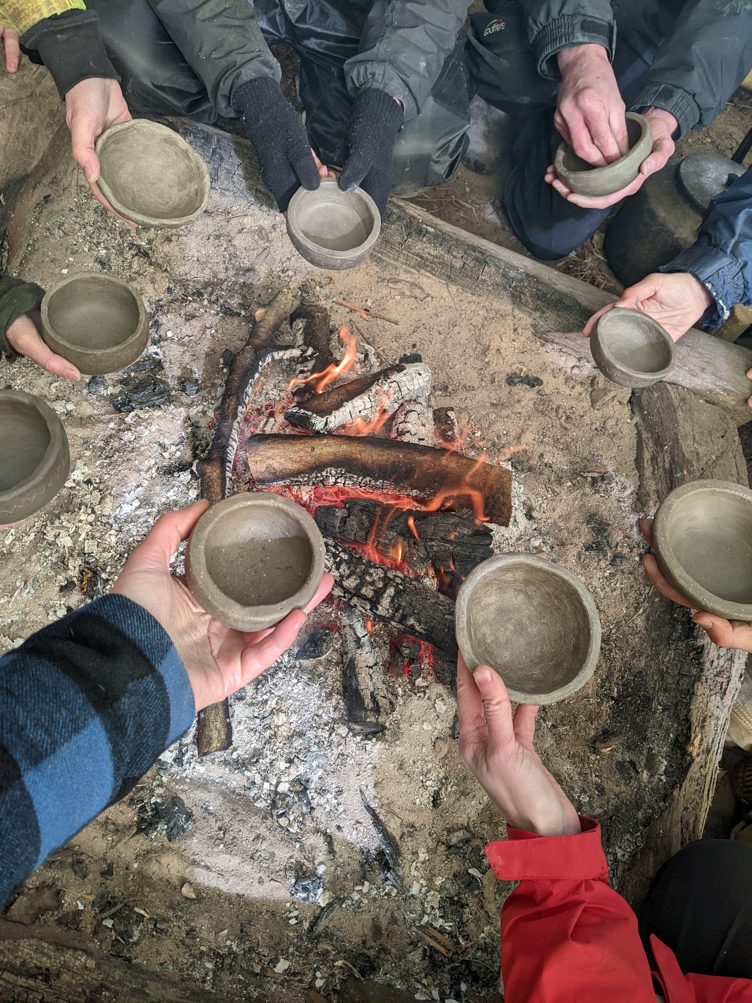 hands holding hand-mad bowls over a camp fire